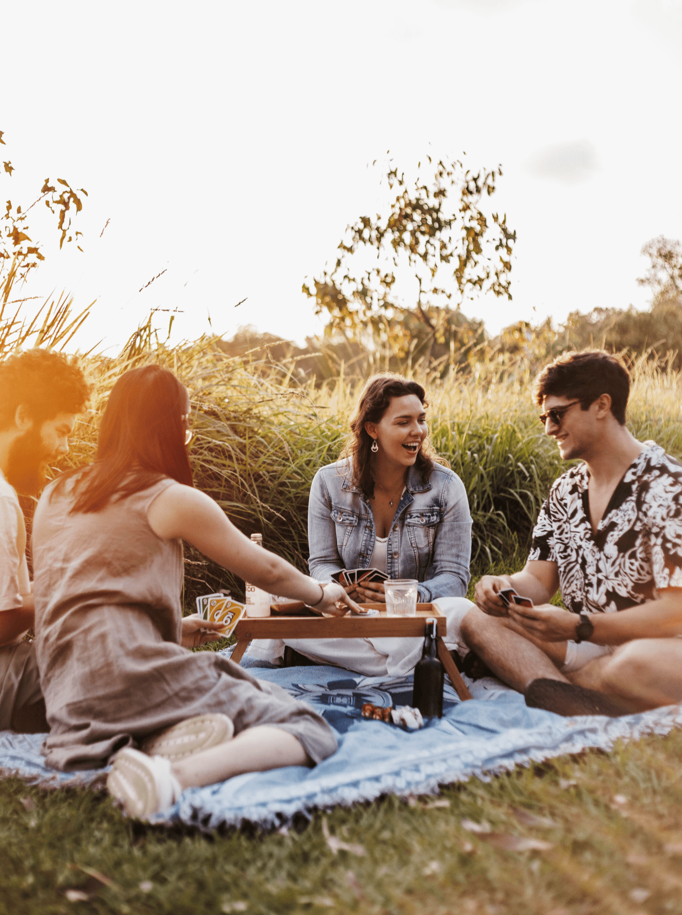 Shooting Stars blue throw rug, picnic blanket laying on grass overlooking sunset with friend playing uno sitting on rug. Designed in Aus. Large enough for picnic of 4 or more.