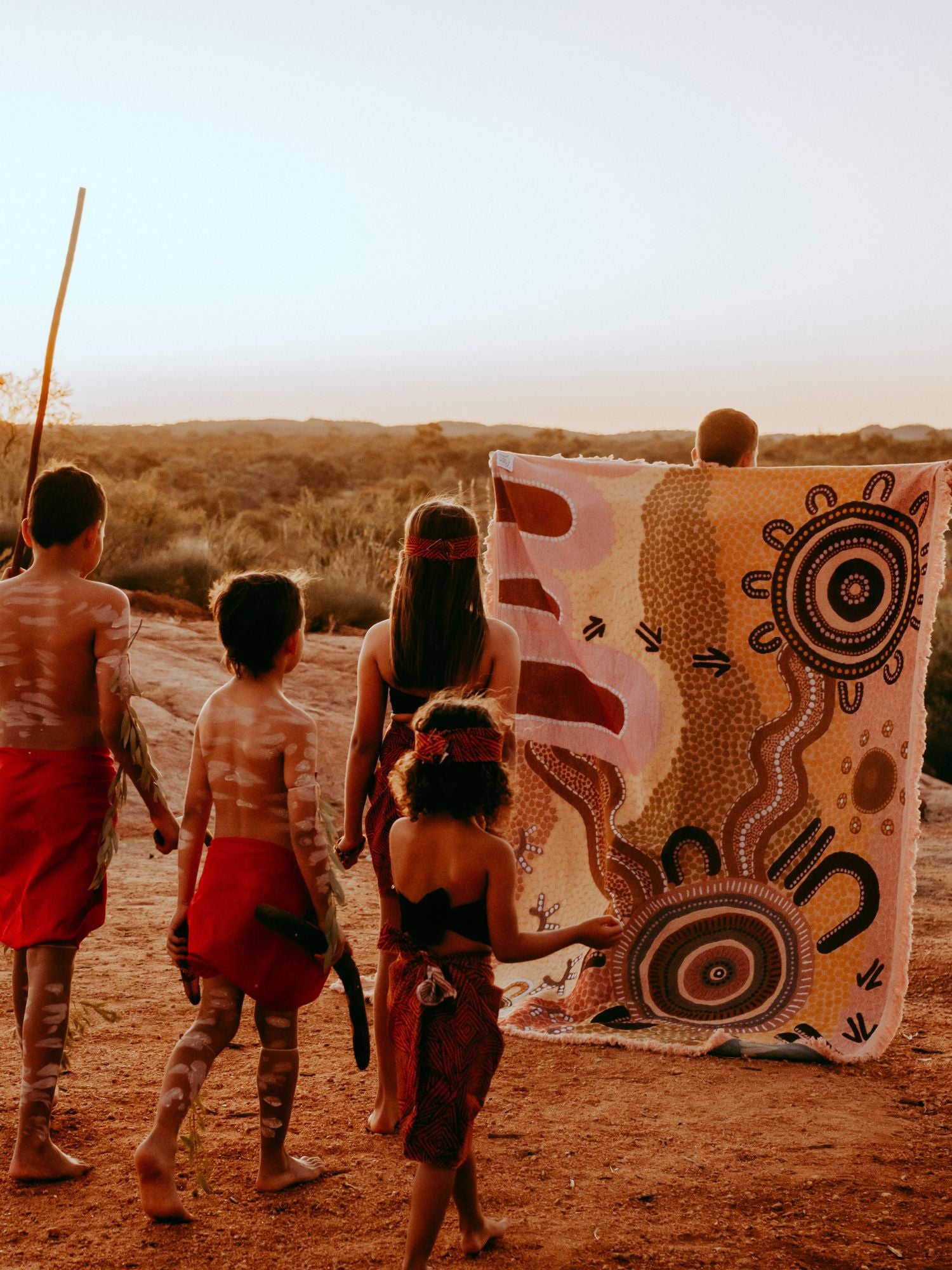 Coming Home Indigenous First Nations art throw rug with Aboriginal children on country. Traditional dress. Blanket woven from recycled fabrics. First Nations art, Kalkadoon mob on Kalkadoon Country. Designed in Australia.