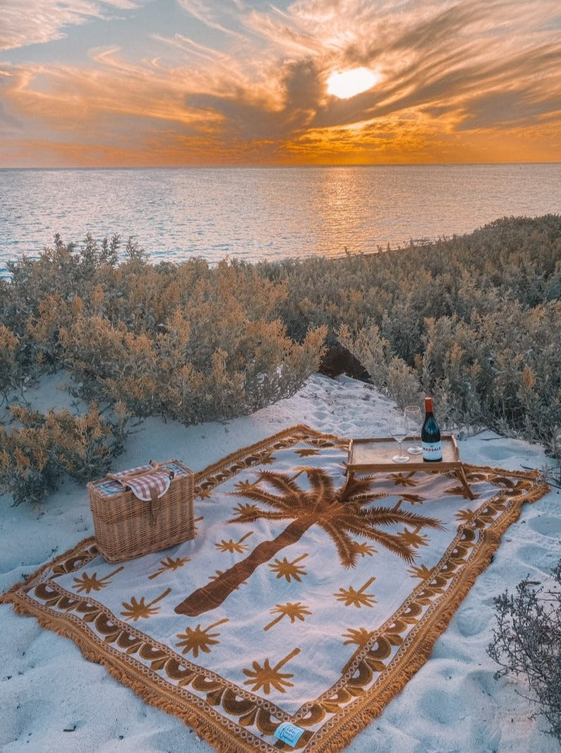 Endless Summer throw blanket spread out on the beach with picnic basket, wine and the sunsetting in the background. Perfect Western Australian evening