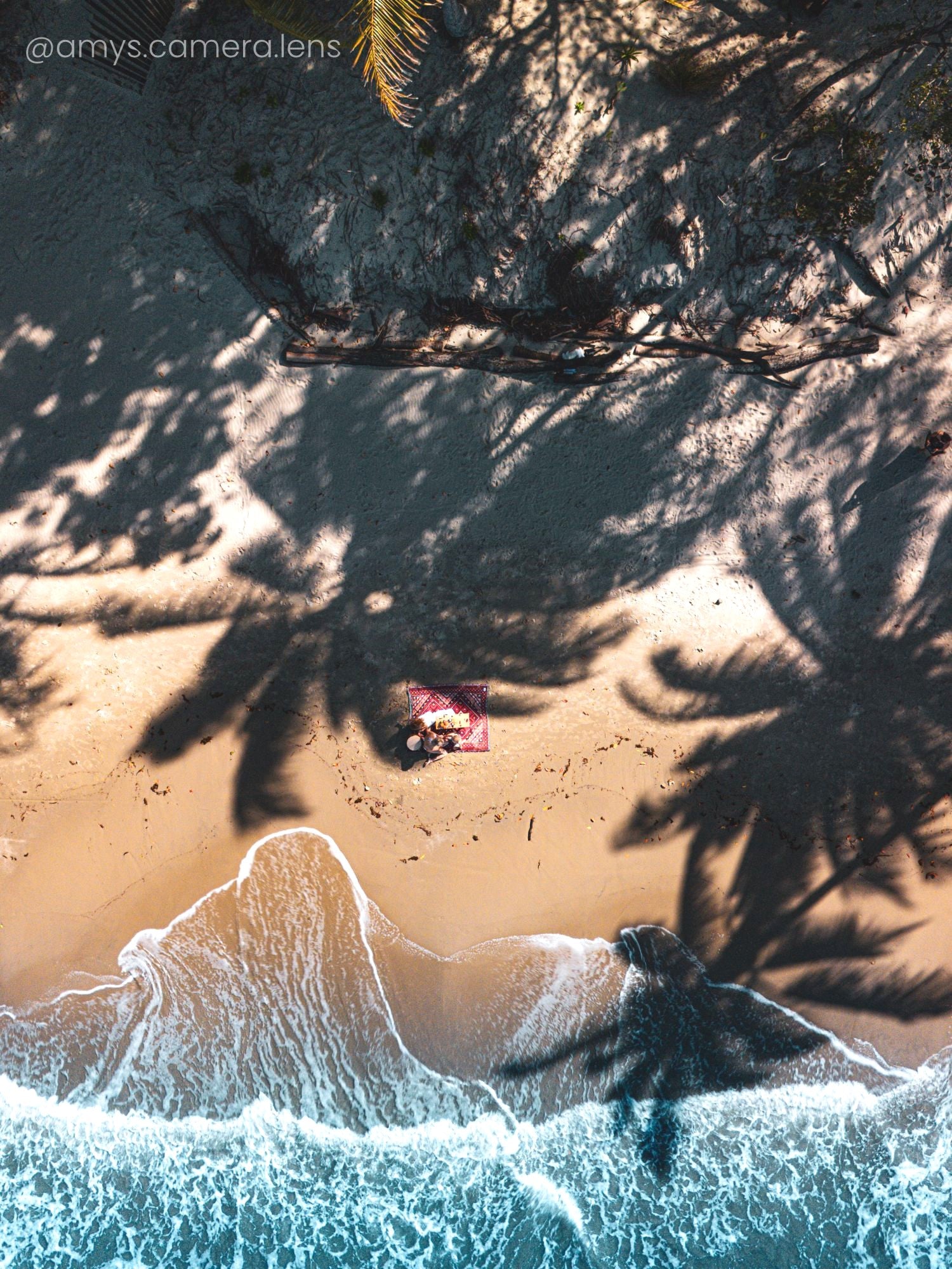 Drone photo of red throw rug Love Lost, beach blanket on sand in Port Douglas with crystal blue waves lapping