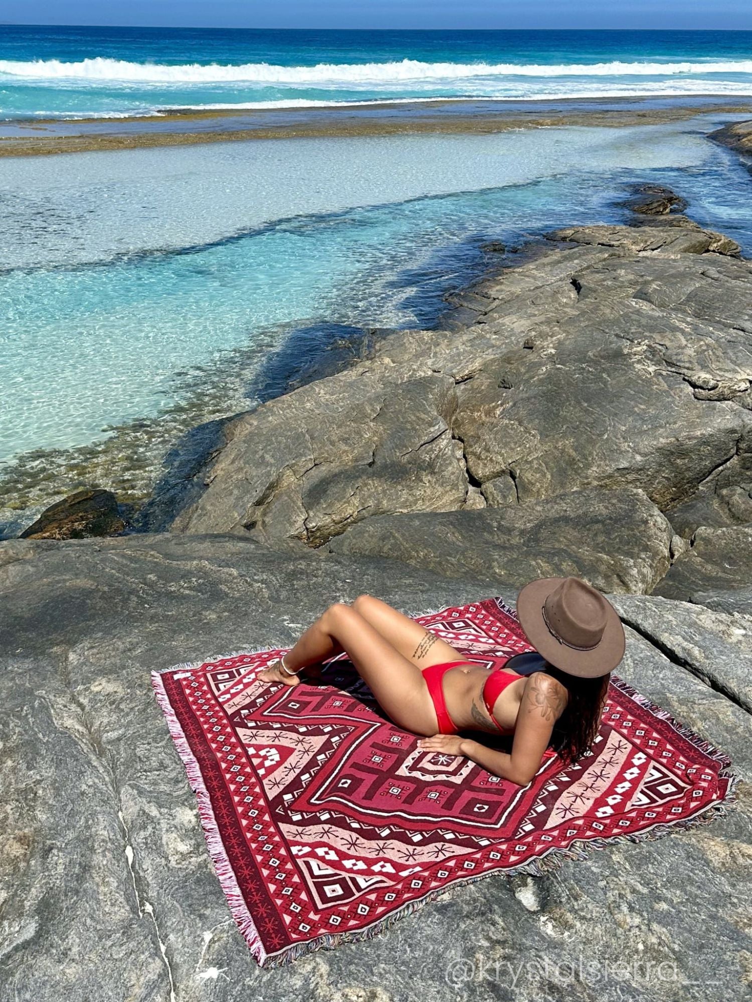 Red throw rug, beach blanket on rocks overlooking crystal blue water in Western Australia.