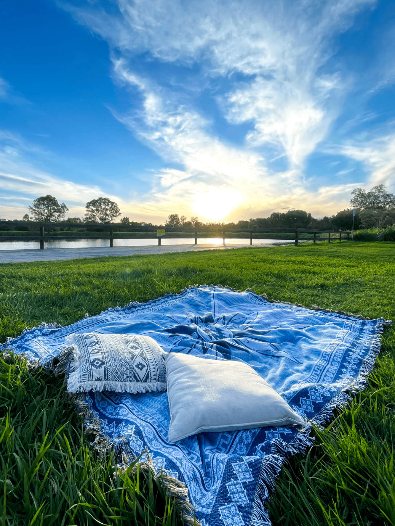 Shooting Stars blue throw rug, picnic blanket laying on grass overlooking sunset. Designed in Aus.