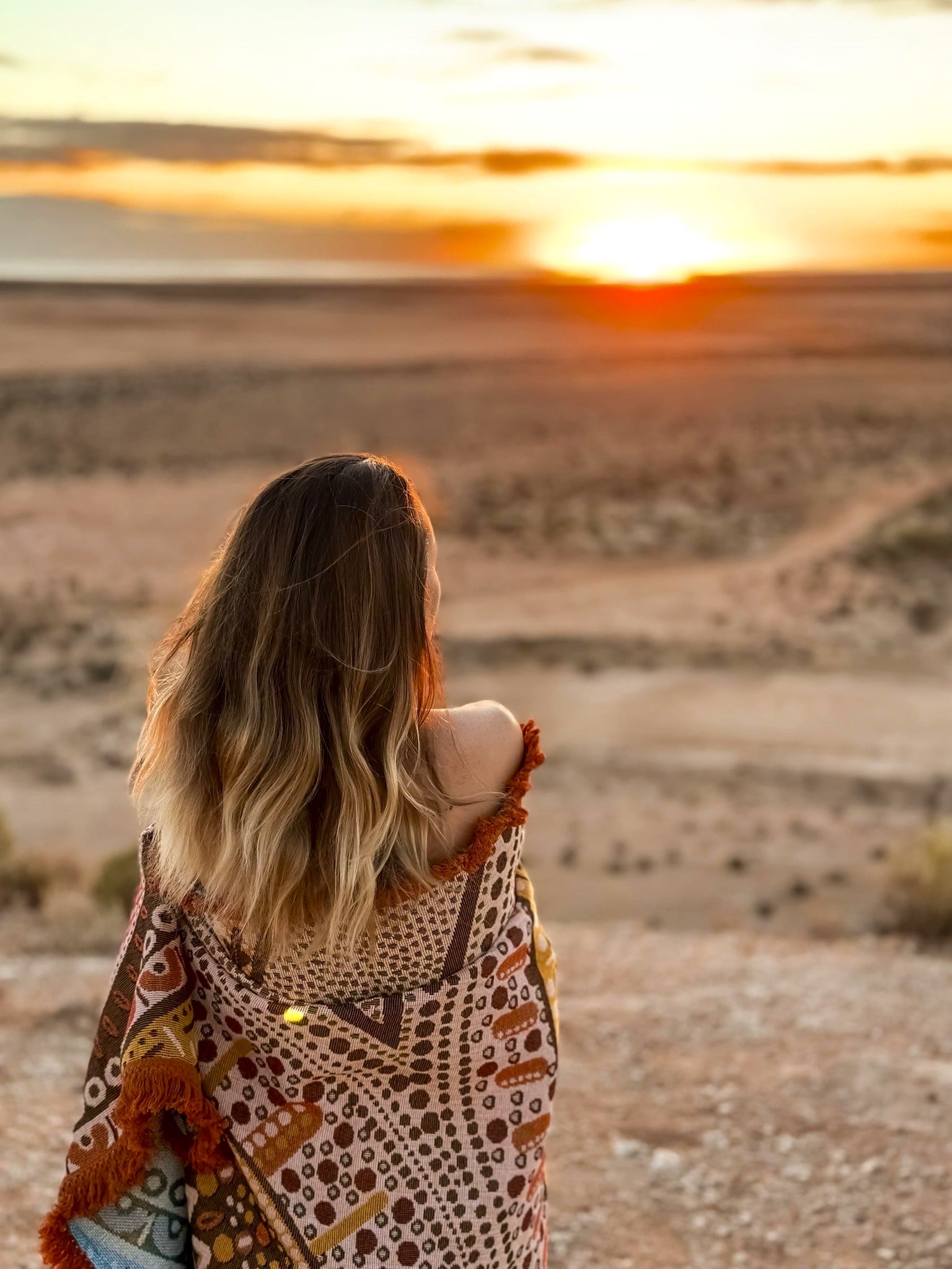 Close up of Stomping Ground throw design details. Indigenous Aboriginal art blanket or rug wrapped around woman watching sunset in Western Australia