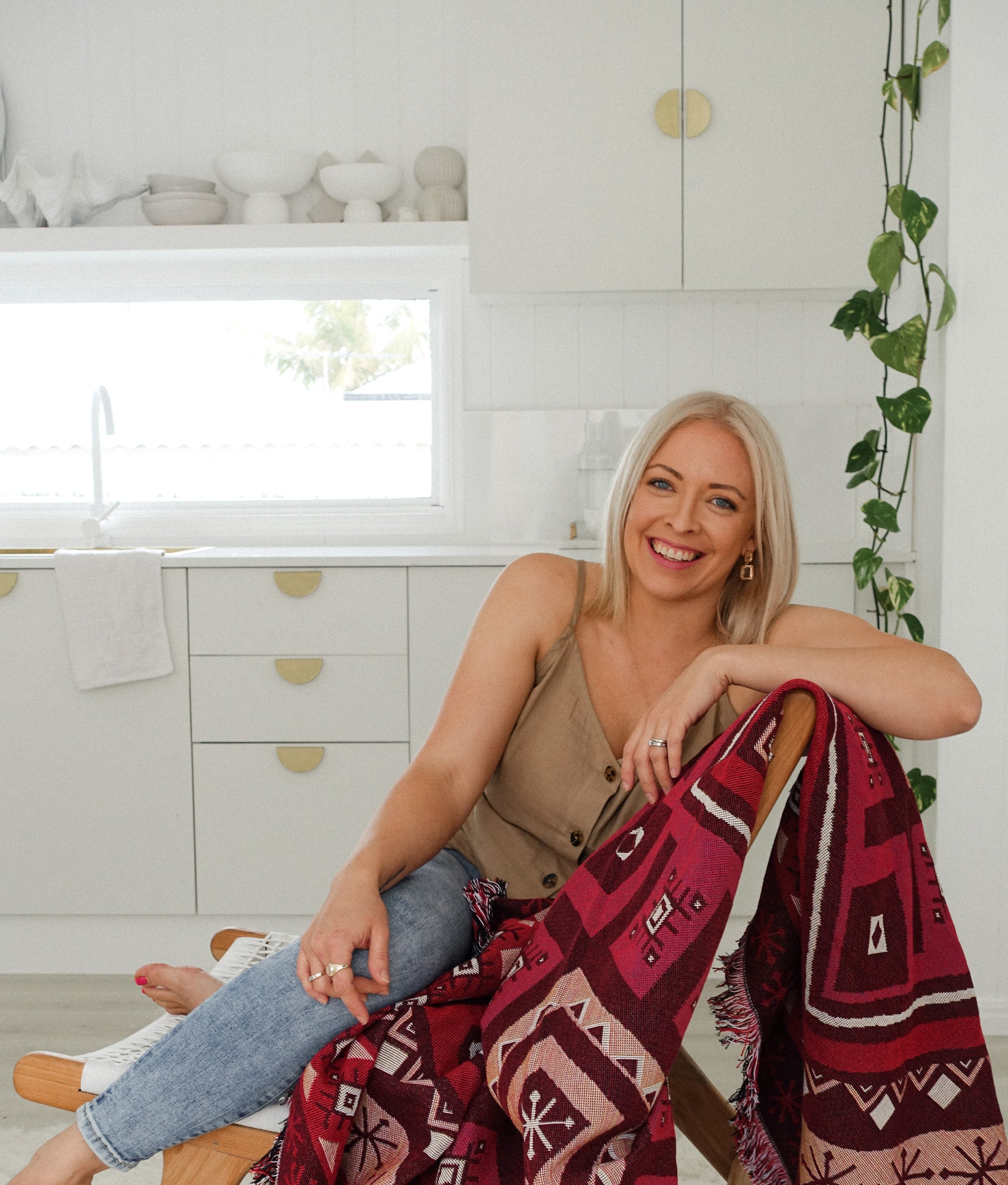 Five Hearts owner and designer, Steph, seated on a chair with her Love Lost red toned throw draped over it.