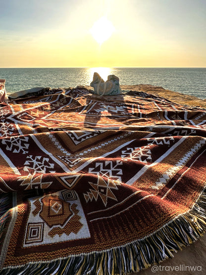 Desert Night throw rug and picnic blanket laying on rocks by ocean at sunset. Shades of brown, boho rug, daily accessory. Designed in Australia for adventure.